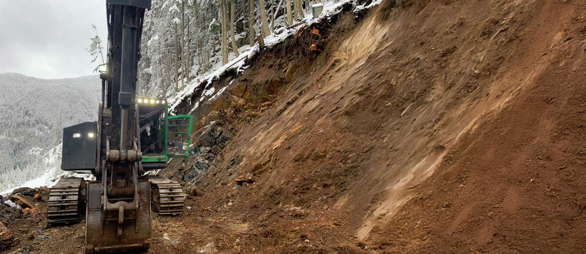 coast-roads-construction-excavator-hillside-snow Excavator working on snowy hillside